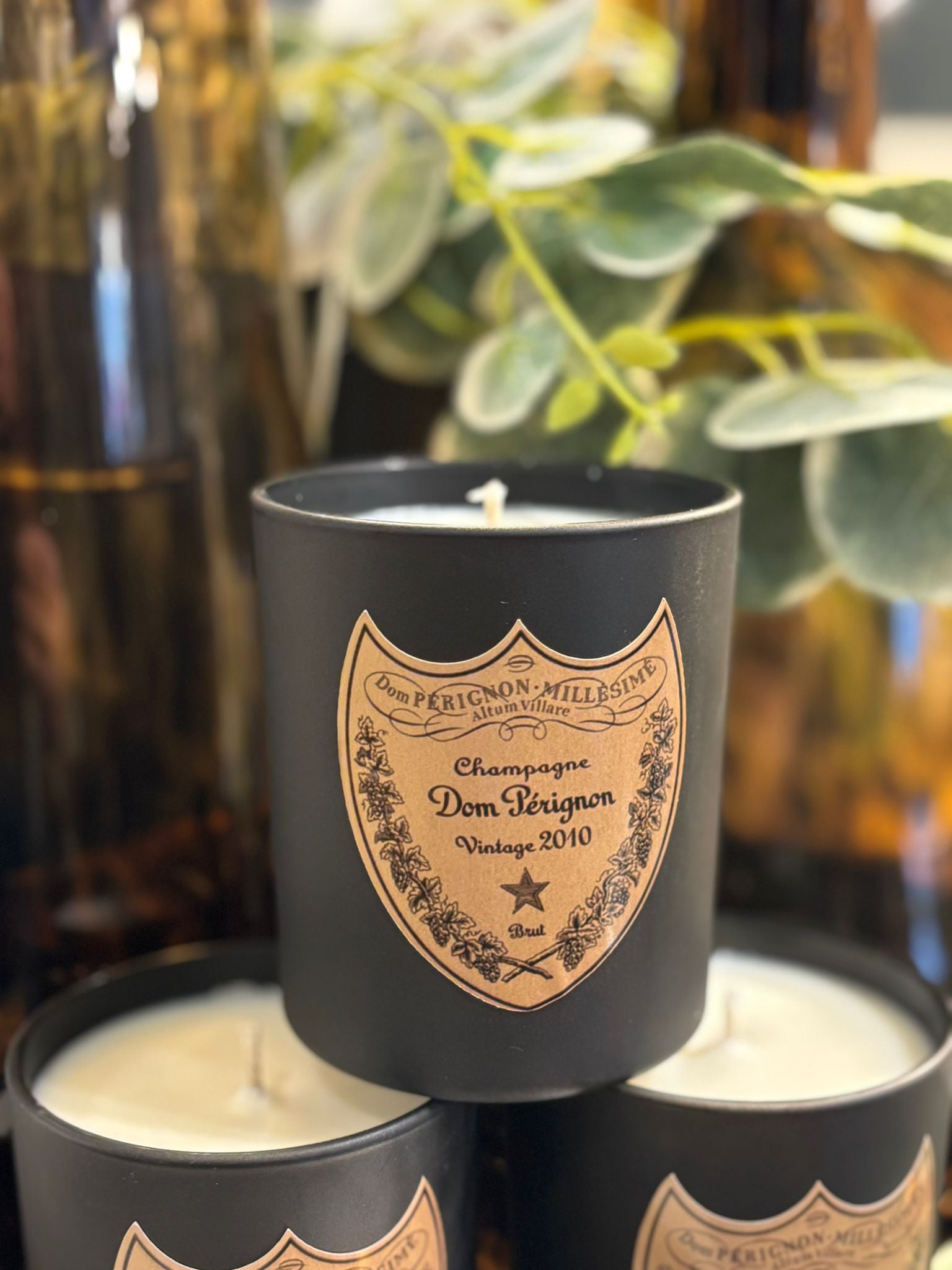 Black Dom Perignon candle with a decorative label in front of green foliage.